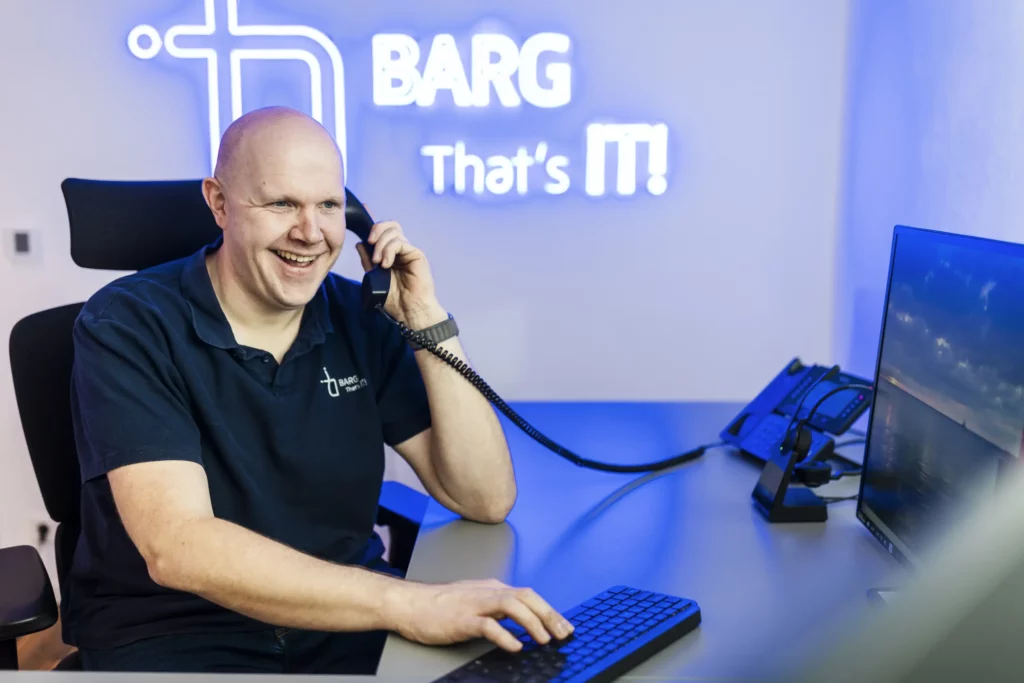 Mann mit Headset sitzt lächelnd am Schreibtisch und telefoniert