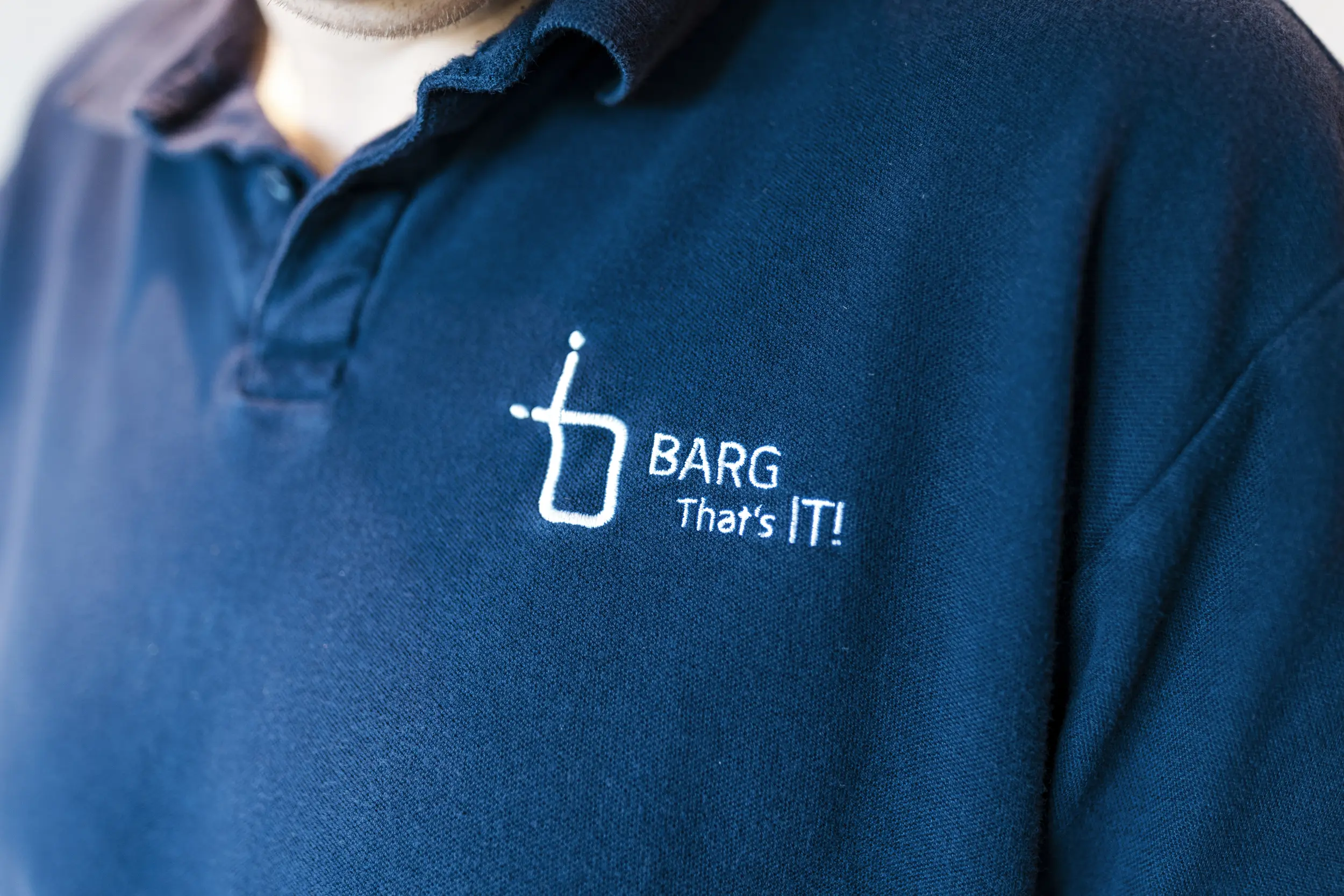 Nahaufnahme eines dunkelblauen Polohemds mit Logo „BARG That’s IT!“