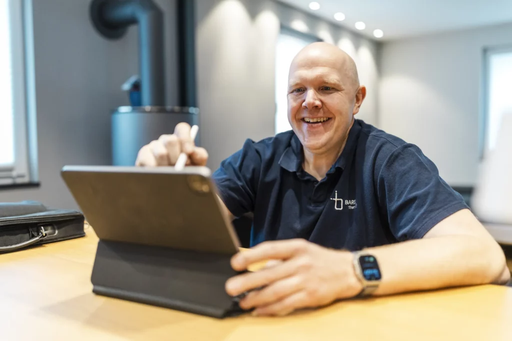 Mann sitzt an Tisch und arbeitet auf einem Tablet